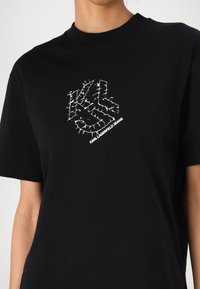 Must musta särk lühikeste varrukatega, mille esipinnal on valge graafiline disain, mis koosneb tähtedest 'KL' ja tekstist "KARL LAGERFELD JEANS". Puuvillane materjal.