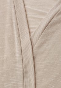Tissu tricoté beige avec une texture côtelée fine et des plis superposés formant un motif en V.