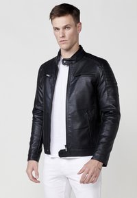 Giacca da moto in pelle nera con colletto rialzato, dettagli trapuntati sulle spalle, cerniere frontali e tasche laterali; texture liscia, design aderente.