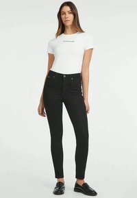 Črne skinny jeans hlače z visokim pasom, izdelane iz denima, z klasičnim zapiranjem na gumb in zadrgo ter zasnovo s petimi žepi.