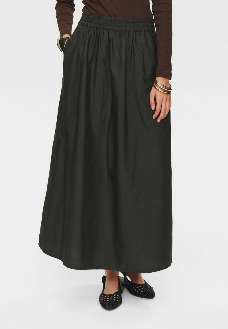 Zwarte, enkellange rok met een elastische tailleband, zijzakken en een gladde stofstructuur. Gecombineerd met geweven zwarte schoenen.