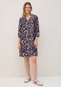 Vestido de manga corta en púrpura oscuro con un patrón de hojas blancas, con diseño de escote en V. Combinado con zapatillas en beige y púrpura.