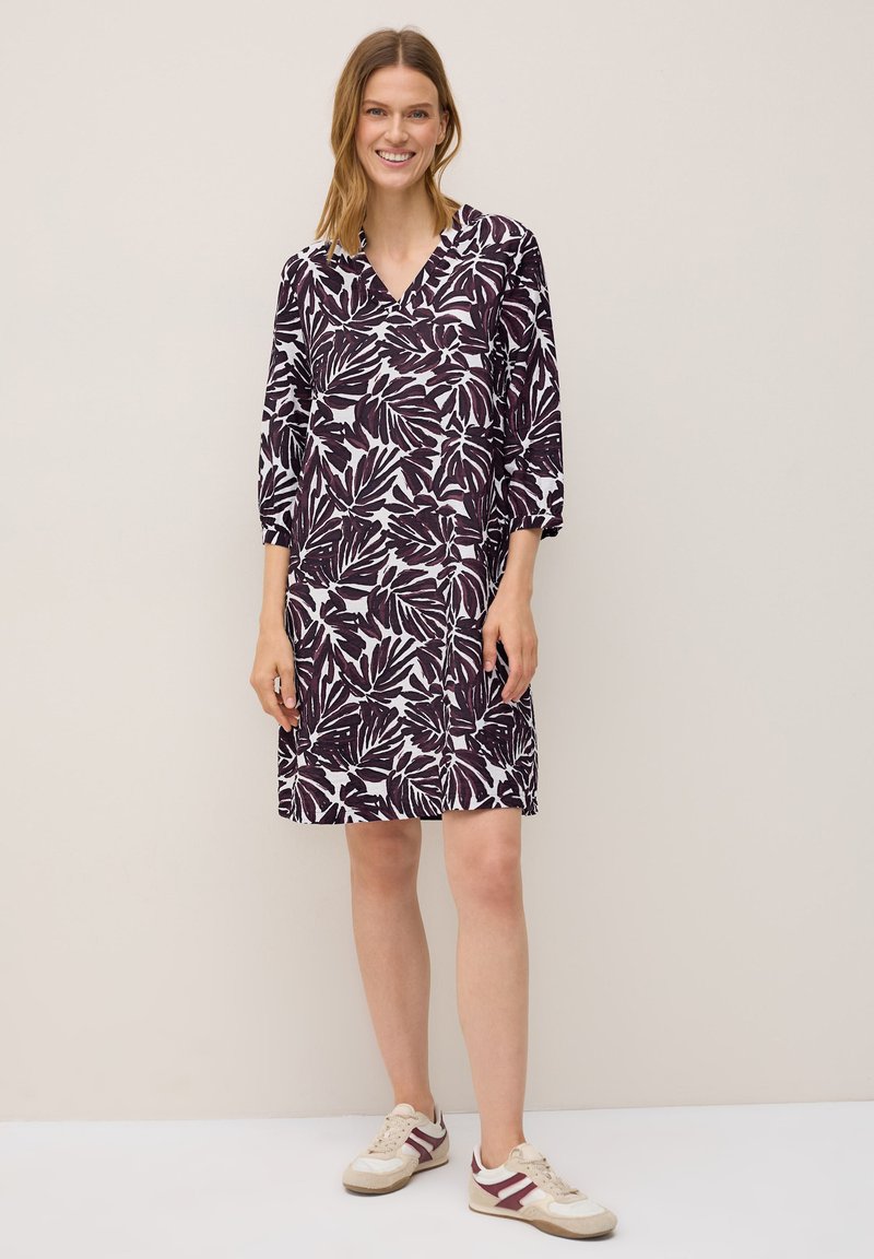Vestido de manga corta en púrpura oscuro con un patrón de hojas blancas, con diseño de escote en V. Combinado con zapatillas en beige y púrpura.