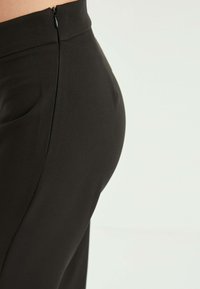 Svarta skräddarsydda byxor med en mjuk textur, hög midja, med en diskret dragkedjestängning bak och en figurnära siluett.