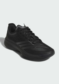 Chaussure de sport noire avec une tige en mesh, surface texturée et rayures contrastantes. Dispose d'une semelle rembourrée et d'une semelle extérieure en caoutchouc durable.