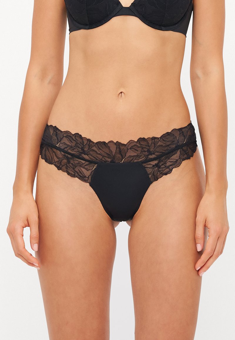 Schwarzer Spitzen-Damenstring mit floralem Design am Hüftbund, der mit transparenter Spitze überzogen ist und eine mittlere Panel aus festem schwarzem Baumwollstoff hat.