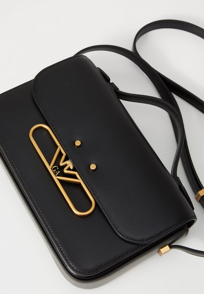 Borsa a tracolla in pelle nera con chiusura in metallo dorato e logo. Presenta un design piatto, tracolla regolabile e una texture liscia.