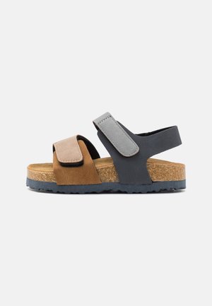 Børnesandal med åben tå med brun frontrem, grå ankelrem, korkindlæg og sort tekstureret sål, vist i sideprofil.