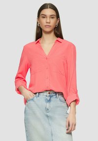 Camicia button-up rosa corallo con scollo a V, due tasche frontali e maniche arrotolate, abbinata a una gonna di jeans azzurro chiaro.