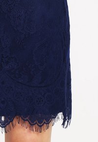 Marinblå spetskjol med intrikata blommönster, vågig nederkant och fransdetaljer längst ner.