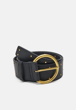 Ceinture en cuir noir avec de petits clous dorés et une grande boucle ronde dorée, enroulée sur un fond clair uni.