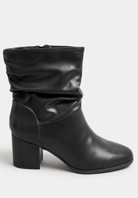 Mustat nahka nilkkurit, joissa on löysä varsi, neliön muotoinen kärki ja paksu korko. Sileä pinta, jossa on minimaalinen ompelutieto. Vetoketjukiinnitys.