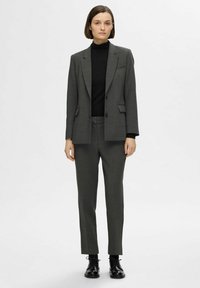 Blazer ajusté gris et pantalon assorti, avec une texture lisse, des revers nets et deux poches avant, associé à un col roulé noir.