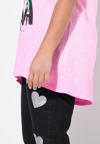 Roze T-shirt met korte mouwen en een licht gebogen zoom, gecombineerd met zwarte jeans met zilveren hartvormige glitteraccenten.