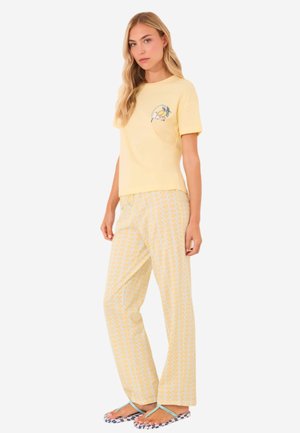 T-shirt en coton jaune à manches courtes avec un design graphique, associé à un pantalon de pyjama blanc orné d'un motif de vagues jaunes répétées.