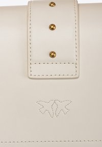 Borse in pelle bianca con finitura texturizzata, borchie oro e logo in rilievo di due uccelli. Cuciture dettagliate lungo i bordi.