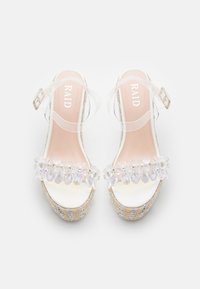 Sandalias de tiras transparentes con plataforma, adornadas con joyas iridiscentes en la puntera. Plantilla suave de color rosa, textura trenzada a lo largo de la suela.