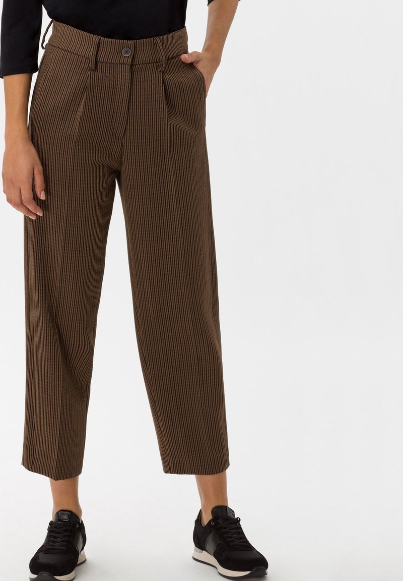 Pantalon rayé marron à taille haute, avec des plis doubles et une fermeture à bouton, associé à des chaussures de sport noires.