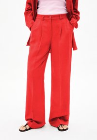 Rode wijdbenige broeken met een gladde textuur, plooien aan de voorkant, hoge taille en zijzakken, gecombineerd met zwarte slippers.