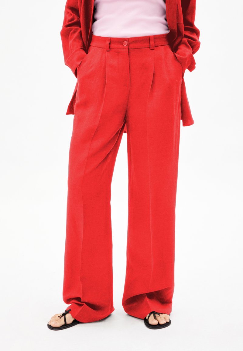 Rode wijdbenige broeken met een gladde textuur, plooien aan de voorkant, hoge taille en zijzakken, gecombineerd met zwarte slippers.