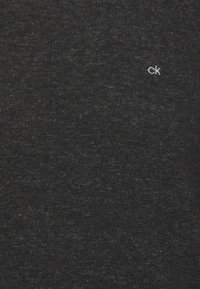 T-shirt nera a collo normale realizzata in morbido cotone misto, con un piccolo logo "ck" bianco sul lato sinistro del petto. Leggera texture su tutta la stoffa.