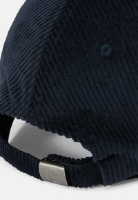 Gorra de béisbol de terciopelo de color navy con textura acanalada, correa ajustable con un gancho de metal y un pequeño detalle de logotipo bordado.