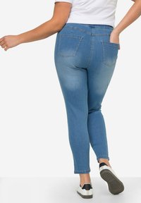 Jeans de mezclilla azul claro con un diseño ajustado, cintura elástica y dos bolsillos traseros. Combinados con zapatillas blancas y negras.