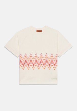 Kremowy T-shirt z krótkim rękawem z zygzakowatym wzorem w odcieniach czerwieni i pomarańczy na wysokości klatki piersiowej oraz małym logo marki blisko dolnego brzegu.