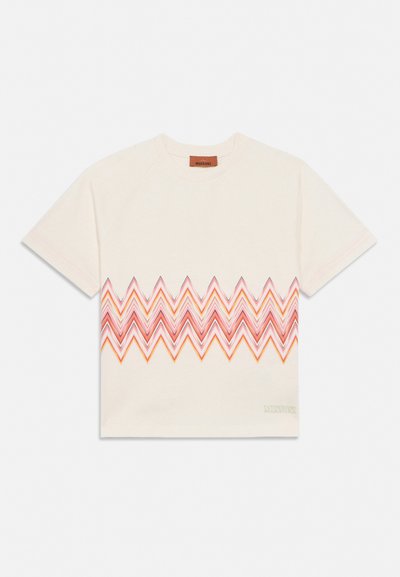 Μπεζ κοντομάνικη μπλούζα με ζιγκζαγκ μοτίβο σε αποχρώσεις κόκκινου και πορτοκαλί στο στήθος και μικρό λογότυπο της μάρκας κοντά στο κάτω μέρος.