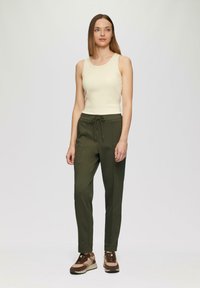 Beige tanktop en olijfgroene joggers met trekkoord, gecombineerd met bruine en tan sneakers. Glad materiaal met een aangesloten ontwerp.
