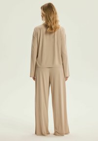 Beżowa, luźna bluzka i szerokie spodnie, obie wykonane z gładkiego materiału. Bluzka ma okrągły dół i opuszczone ramiona.
