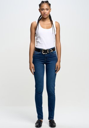 Jeans in denim dritto di colore blu scuro con una leggera elasticità. Abbinati a una canotta bianca aderente e una cintura nera con fibbia argentata.