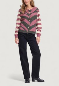 Cardigan lavorato a maglia con motivo a zigzag rosa e grigio, strisce crema e bottoni a forma di cuore. Abbinato a pantaloni neri a gamba larga e stivali con tacco.