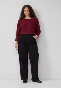 Burgundowa bluzka z długim rękawem i szerokim dekoltem, zestawiona z czarnymi jeansami o wysokim stanie. Obie części wykonane są z miękkich, fakturowanych tkanin.