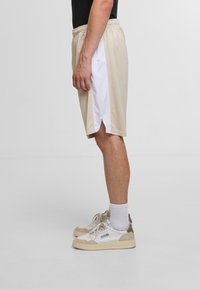 Herren beigen Sportshorts aus Mesh mit einem weißen seitlichen Einsatz, ausgestattet mit einem elastischen Bund und seitlichen Schlitzen für Bewegungsfreiheit.