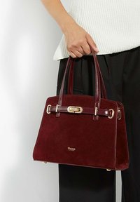 Burgundy suede handbag with gold hardware, structured design, short handles, and a logo at the base. Textured surface with shiny accents.