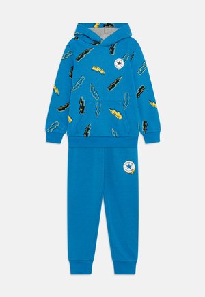 Completo felpa blu e pantaloni con motivi di fulmini in nero e giallo. La felpa ha una tasca frontale e il logo a stella sui pantaloni.