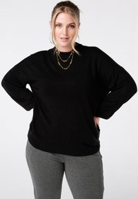 Zwarte gebreide trui met een losse pasvorm, brede mouwen en een ronde hals, gecombineerd met grijze leggings. Gladde textuur, geen zichtbare patronen.