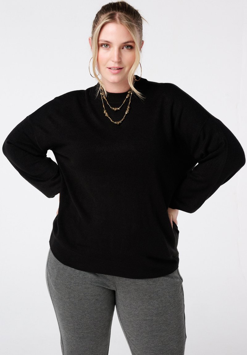 Zwarte gebreide trui met een losse pasvorm, brede mouwen en een ronde hals, gecombineerd met grijze leggings. Gladde textuur, geen zichtbare patronen.