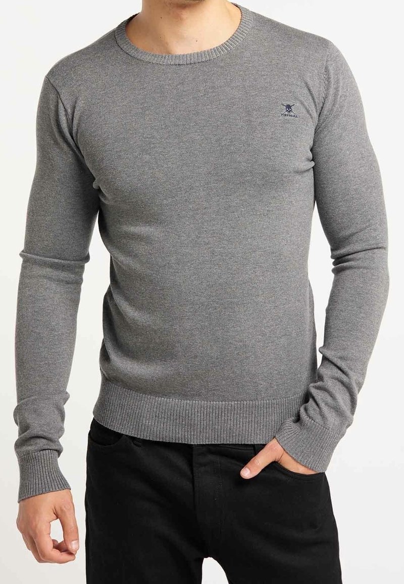 Pull gris tricoté avec manches longues, encolure arrondie, poignets et ourlet côtelés, et un petit logo brodé sur la poitrine.