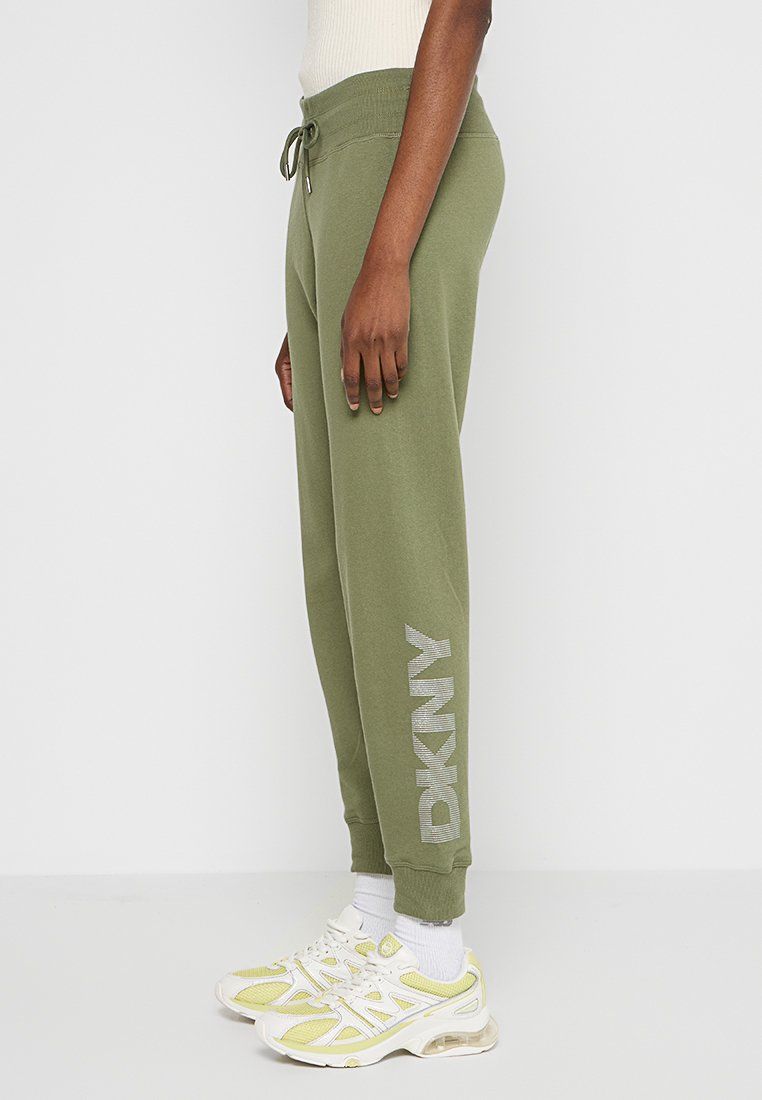 Pantaloni della tuta verde oliva con vita aderente, coulisse e il logo 'DKNY' in grigio chiaro lungo la gamba inferiore. Tessuto morbido.
