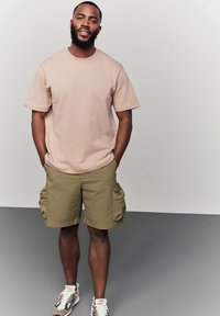Light beige short-sleeve T-shirt, olive green cargo shorts with side pockets, and multi-color athletic shoes on a gray background.