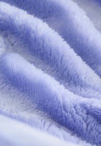 Couverture en peluche violette avec une texture douce et moelleuse, présentant des ondulations et des plis qui accentuent son épaisseur et sa chaleur. Aucune motif ou élément matériel visible.