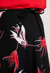 Gonna nera con un motivo floreale rosso e bianco. Vita con laccetto nero. Texture liscia, vista ravvicinata dei dettagli del design.