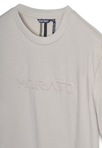 T-shirt a girocollo beige chiaro con testo in rilievo "MORATO" e un'etichetta nera all'interno del colletto che riporta "ANTONY MORATO RELAXED-FIT."