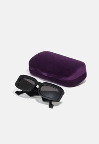 Ochelari de soare negri cu un cadru geometric, lentile închise la culoare și brațe texturate, însoțiți de un toc din catifea purpurie.