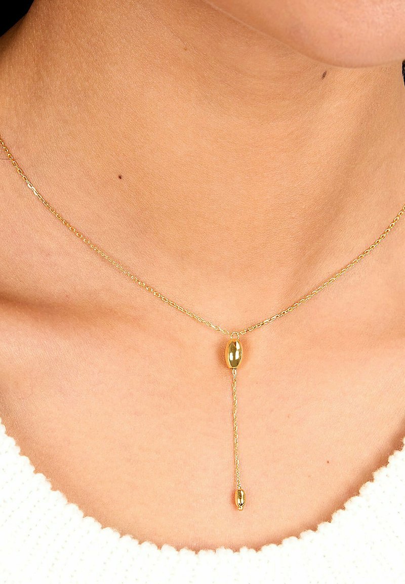 Gul vedhæng halskæde med en delikat kæde, der har en oval centerperle og en hængende kædeaccent. Glat tekstur og blank finish.