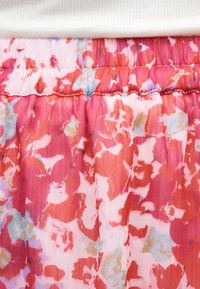 Κοντινό πλάνο ροζ υφάσματος με κόκκινα, λευκά και ανοιχτό μπλε λουλουδένια μοτίβα και ελαστική μέση κάτω από ένα λευκό ριμπ ύφασμα.