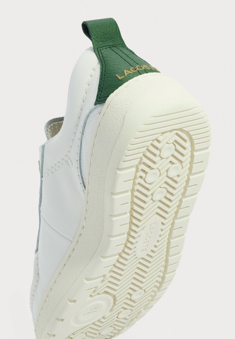 Baskets blanches avec un empiècement en cuir vert au talon. Semelle en caoutchouc texturé avec un motif en chevron. Tige lisse avec détails de couture.