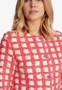 Sakko aus Tweed mit einem karierten Muster in Rosa und Weiß mit bunten Sprenkeln. Mit runden, rosa Knöpfen geschlossen und einer strukturierten Oberfläche.